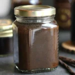 Homemade vanilla bean paste in a glass jar with fresh vanilla pods on a wooden table