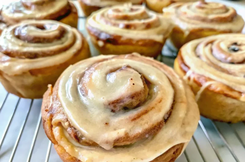 Homemade cinnamon rolls frosting being drizzled over warm pastries with cream cheese icing