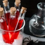 Test tubes filled with red Halloween drinks and eyeball candy, placed in a glass of dry ice with spooky decor.